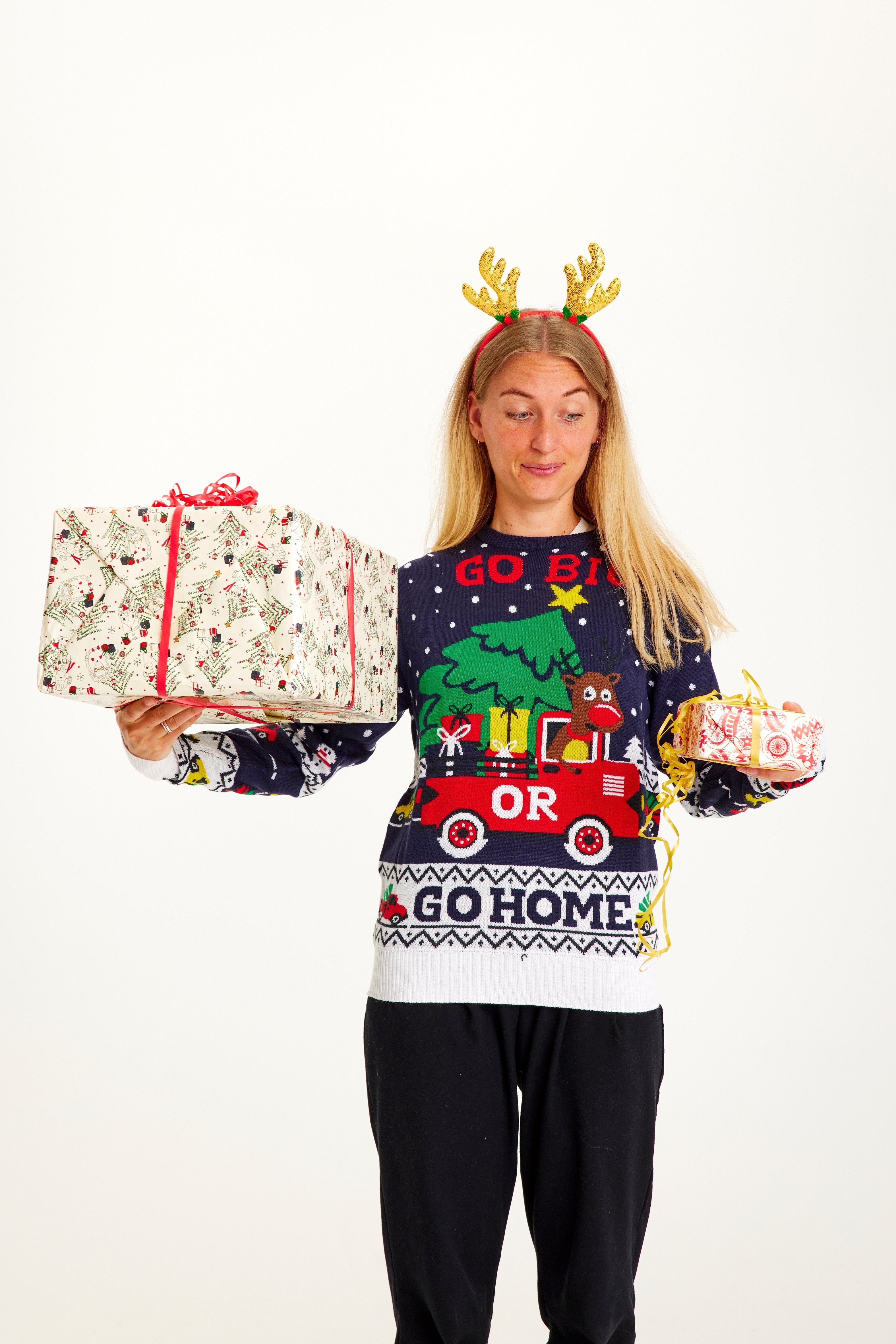 Eine Frau posiert mit Weihnachtsgeschenken und trägt einen weißen und blauen Weihnachtspulli.